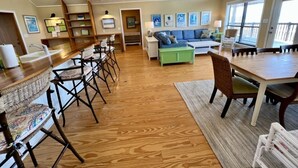 Amplia sala de estar con piso de madera, una mesa de comedor, un sofá y una zona de cocina con barra.