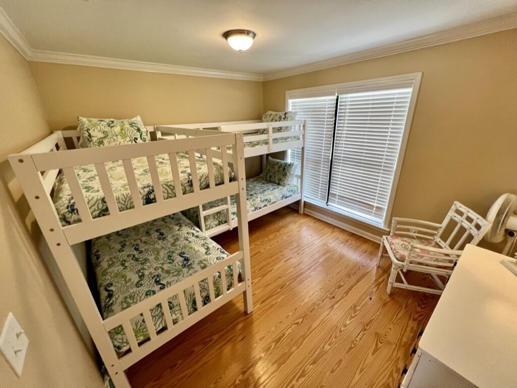 A room with two bunk beds, a white chair, and a window with blinds.