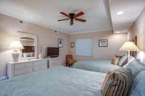 Une chambre avec deux lits, un ventilateur de plafond, une commode, un téléviseur et une fenêtre avec des stores.