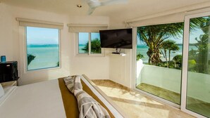 Una habitación de hotel con una cama, televisión y balcón con vista al océano.