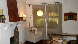 A cozy living room with a fireplace, a comfortable armchair, a table with books, and a decorative mirror. - Beautiful Cozy Bedroom In Great B&B  Historic Home ~ Close To The City Center  (Miami)