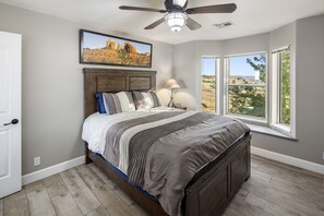 Ein Schlafzimmer mit einem Bett, einem Deckenventilator, einem Fenster mit Aussicht und einem gerahmten Bild an der Wand.