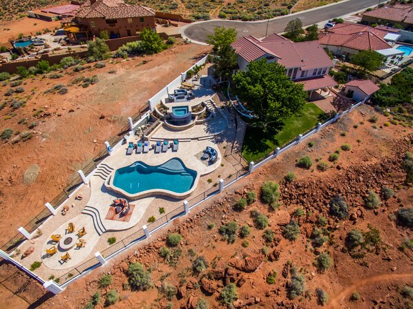 Eine Vogelperspektive zeigt ein Resort mit großem Schwimmbecken, Liegestühlen und einem gepflegten Rasen.