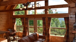 Una cabaña acogedora con interior de madera, un sofá de cuero, una mesa de comedor y grandes ventanales con vistas al exterior.