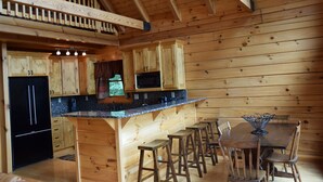 Interior de una cabaña de madera con cocina, comedor y un balcón.