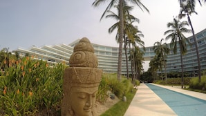Et moderne hotel med stor swimmingpool, palmer og en dekorativ stenskulptur.