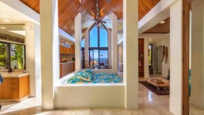 Una habitación amplia con techo alto, un ventanal grande y una cama con cubrecama de temática tropical.