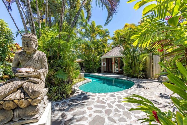 Una estatua de una figura sentada en un jardín tropical con una piscina.
