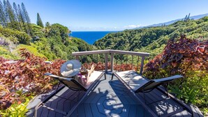 Una terraza con dos sillones y una mesa, con vista a un valle exuberante y el océano.