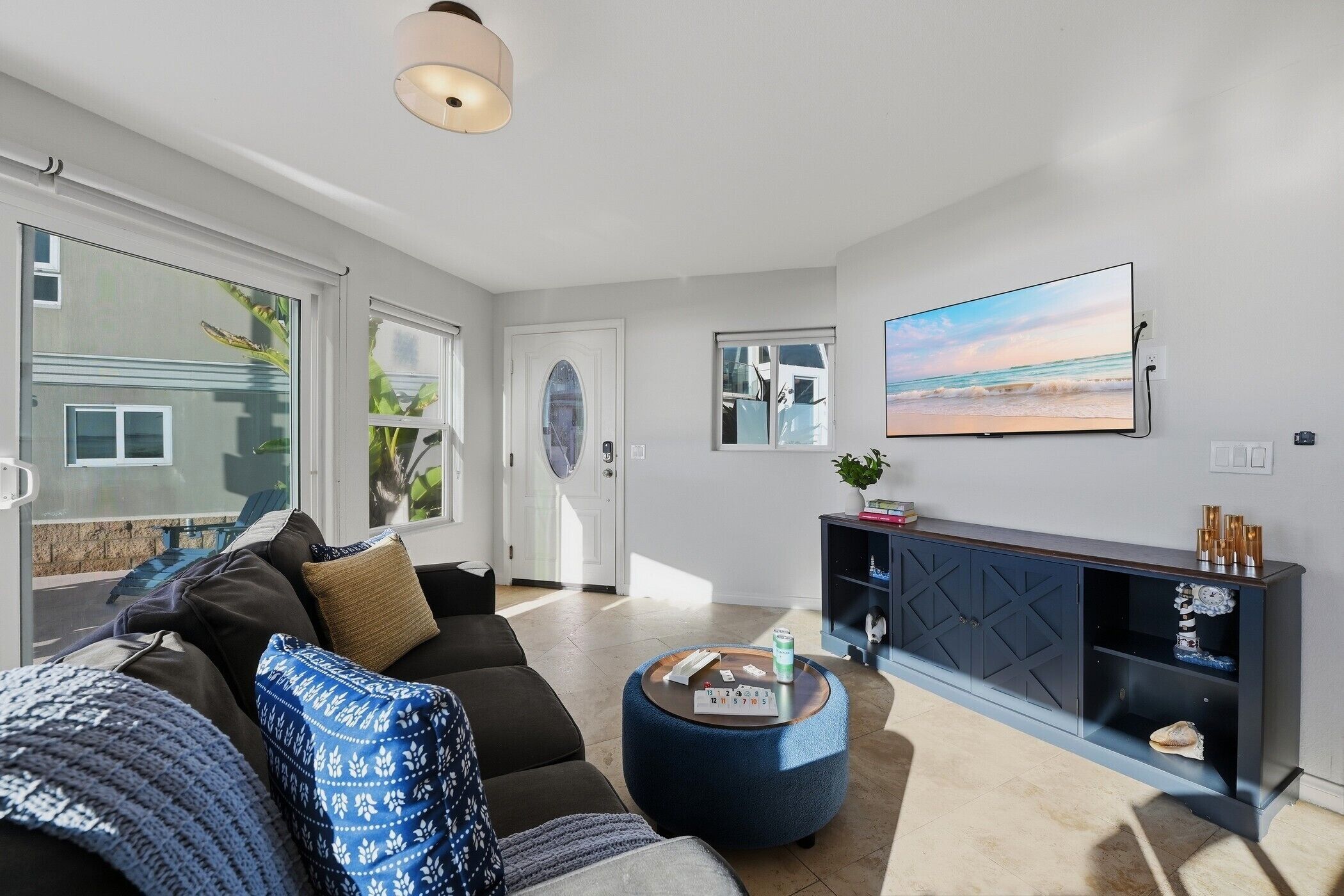 A modern living room with a sofa, ottoman, and a flat-screen TV mounted on the wall.