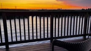 A wooden deck with a railing overlooking a body of water, with a chair and a table.