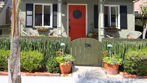 Una casa con puerta roja, plantas en macetas y un pequeño porche.