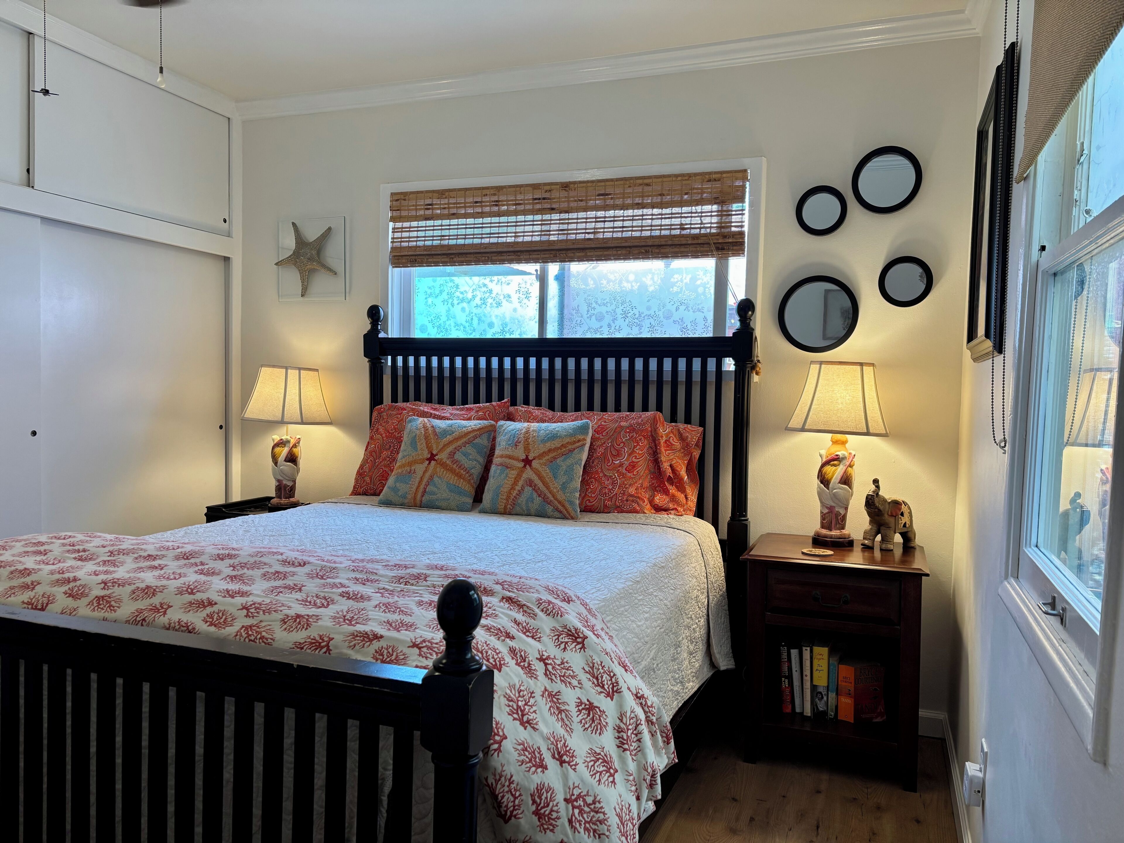 A neatly arranged bedroom with a bed, bedside lamps, a nightstand with books, and a window with blinds.
