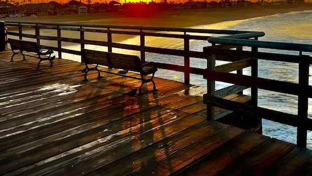 Un muelle de madera con bancos que da a una playa al atardecer.