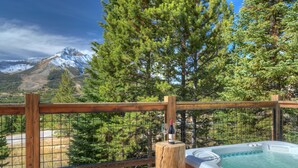 A wooden deck with a hot tub and a bottle of wine, overlooking a mountainous landscape.