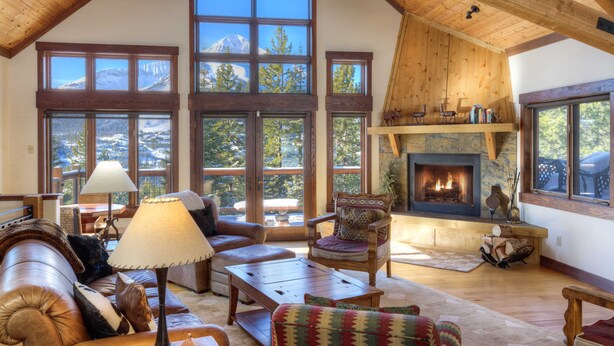 A spacious living room with large windows, a fireplace, and a high ceiling with exposed beams.