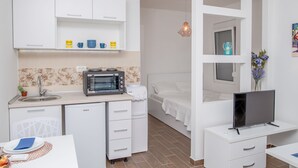 Kompakti hotellihuone, jossa on pieni keittiönurkkaus, sänky, televisio ja pieni ruokailutila.