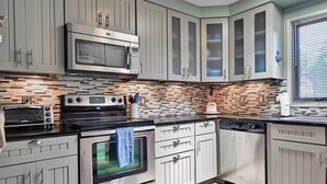 Une cuisine moderne dotée d’appareils électroménagers en acier inoxydable, d  ’un pare-feu en carrelage et de meubles de couleur claire.
