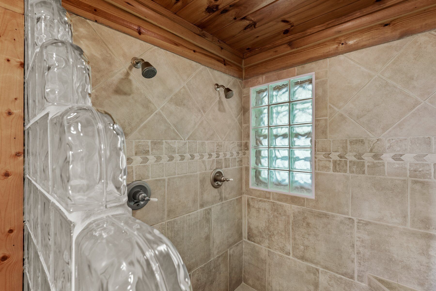 Une douche avec un plafond en bois et des murs carrelés, une fenêtre en verre dépoli et un pommeau de douche.