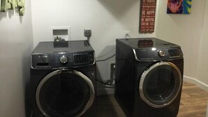 Ein Waschraum mit zwei Waschmaschinen mit Frontlader, einem Samsung Trockner und einem an der Wand befestigten Schild mit Familienregeln.