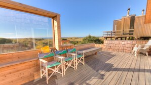 A wooden deck with a view of the beach, a wooden bench, and a table with chairs. - Whimsical Ocean Front Home! Hot tub & Dog Friendly! (Waldport)