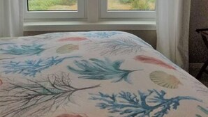 Een kamer met een bed, een raam met gordijnen en uitzicht op groen en water.