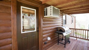A wooden cabin with a front door, a window, a grill, and an air conditioning unit.