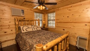 A wooden cabin bedroom with a bed, a ceiling fan, and a window.