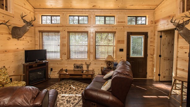 A log cabin interior with a brown leather sofa, a television, and two deer antlers mounted on the walls.