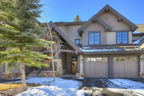 Une maison à deux étages, avec des fondations en pierre, un garage et une allée recouverte de neige.