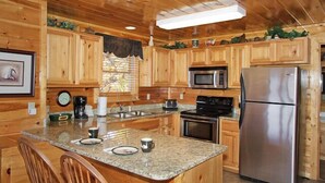 Cocina de cabaña de madera con encimeras de granito, electrodomésticos de acero inoxidable y una isla grande con asientos.