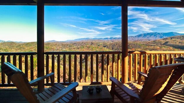 Una terraza de madera con dos sillas y una mesa, con vistas a un paisaje montañoso.