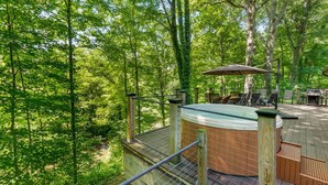 A hot tub on a wooden deck surrounded by trees, with outdoor furniture and a grill. - Secluded Log Cabin Estate | 6 Private Acres | High-Altitude River Views (New Buffalo)