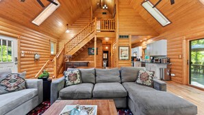 A log cabin interior with a living room, staircase, kitchen, and a balcony. - Secluded Log Cabin Estate | 6 Private Acres | High-Altitude River Views (New Buffalo)