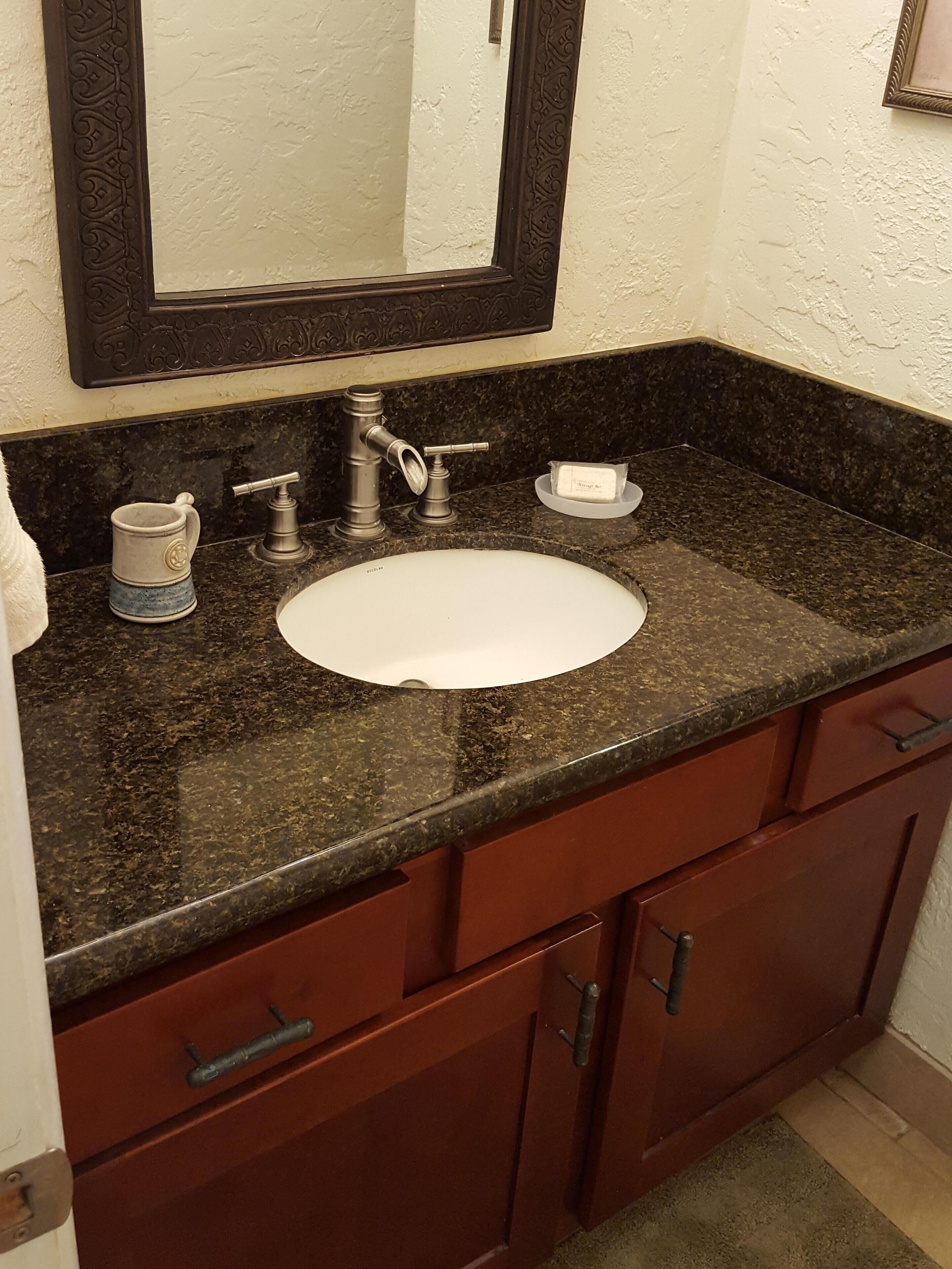Un baño con encimera de mármol, lavamanos blanco, tocador de madera oscura y espejo con marco decorativo.