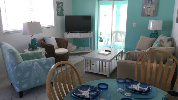 A living room with a television, a dining table with blue glassware, and a 'Welcome to the Beach' sign. - STEPS TO BEACH & STEPS TO BAY & TO WATCH DOLPHINS! 3 MIN WALK TO RESTAURANTS (Englewood)