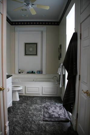 A bathroom with a white bathtub, a toilet, a vanity with a mirror, and a ceiling fan. - Apt. G above G Gallery & Glass Studio in a beautiful 1890 historic building (Guthrie)