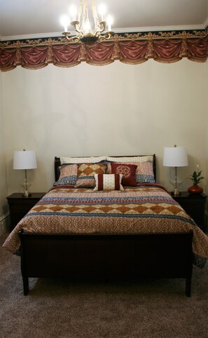 A bedroom with a large bed, two bedside tables with lamps, a chandelier, and a decorative valance. - Apt. G above G Gallery & Glass Studio in a beautiful 1890 historic building (Guthrie)