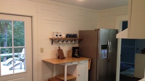 Una cocina compacta con refrigerador, cafetera y un estante con tazas.