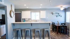 Una cocina con una isla central, taburetes de bar y una zona de comedor con sillas.