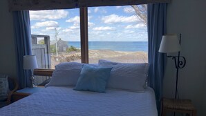 Een slaapkamer met een groot bed, uitzicht op het strand en een lamp op het nachtkastje.