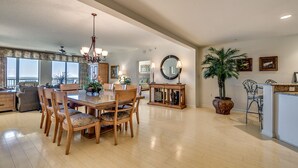 A spacious dining area with a wooden table and chairs, a chandelier, and a large potted plant.