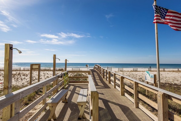 A wooden boardwalk leading to a beach with an American flag.