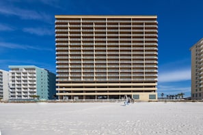 Un hôtel à plusieurs étages dont les balcons présentent un design uniforme, situé à proximité d’une plage de sable.