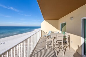 A balcony with a view of the beach, a table with chairs, and a door.