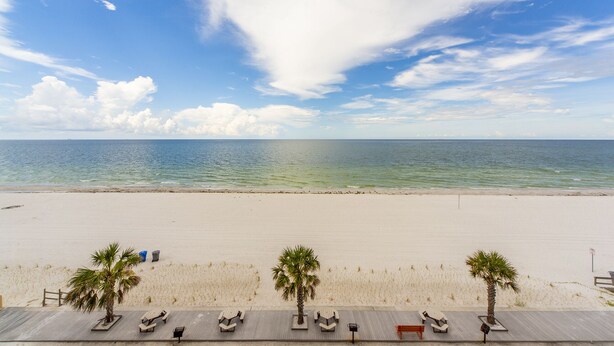 Een strand met een houten terras, palmbomen en een helder uitzicht op de oceaan.