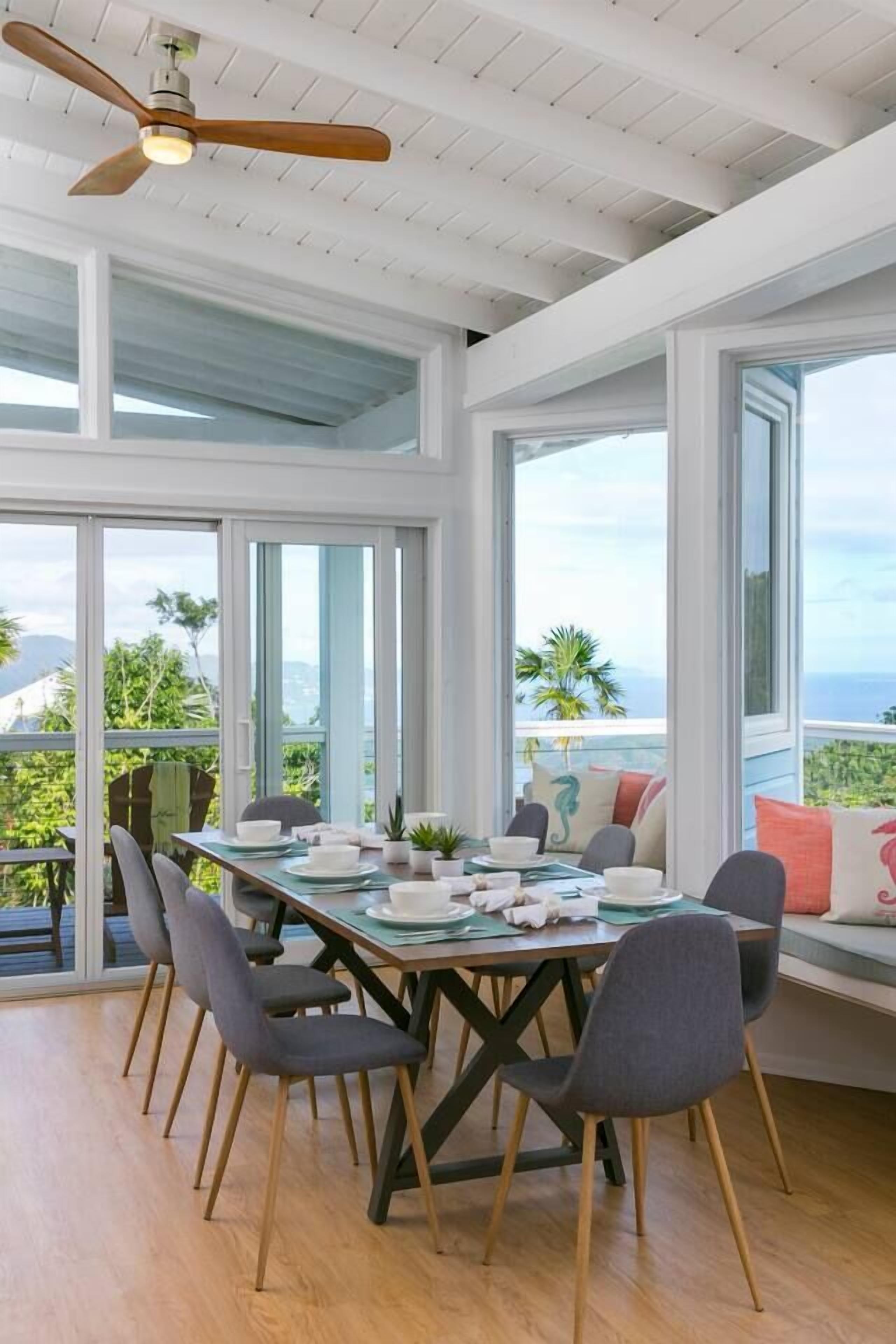 A dining area with a table set for four, large windows, and a ceiling fan.