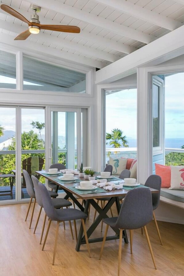 A dining area with a table set for four, large windows, and a ceiling fan.
