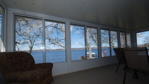 A room with large windows offering a view of a lake and trees. - Lake House with Sandy Beach and Amazing Sunsets (Delton)