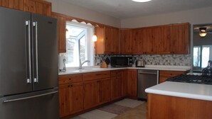 A kitchen with wooden cabinets, a stainless steel refrigerator, a microwave, and a dishwasher. - Lake House with Sandy Beach and Amazing Sunsets (Delton)